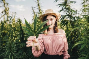 a woman holding up a cannabis leaf in a field of cannabis plants